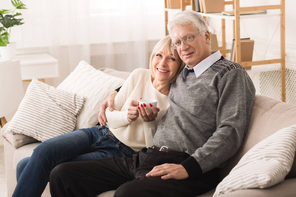 Relaxed senior couple sitting on sofa and looking at camera - Foto, Imagen