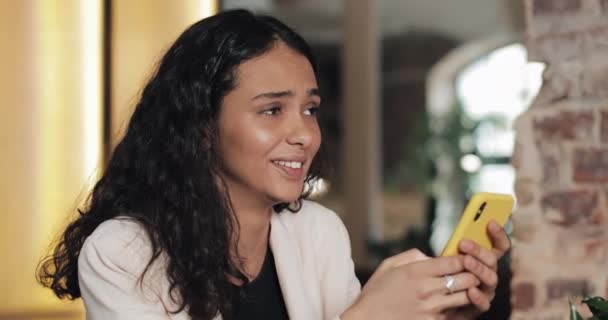 Happy young businesswoman using yellow smartphone chatting in social media sitting in cafe, smiling young woman user holding cellphone reading good news texting receiving message on phone - Video