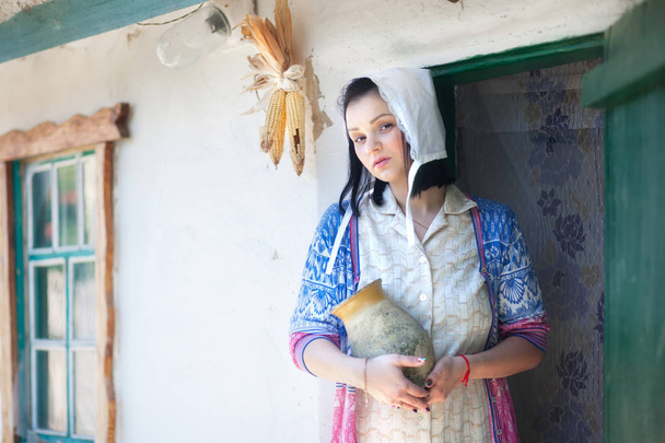 Młoda kobieta na tle retro dom wsi z dzbanem w jej ręce. - Zdjęcie, obraz
