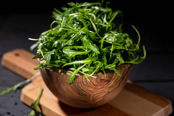 Fresh rucola in the wood bowl full of rocket salad leaves over the black background, selective focus - Φωτογραφία, εικόνα