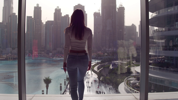 Fiatal nő az ablak jön, és keres, és lenézett a tóra és a részhalmaz felhőkarcolók. - Felvétel, videó