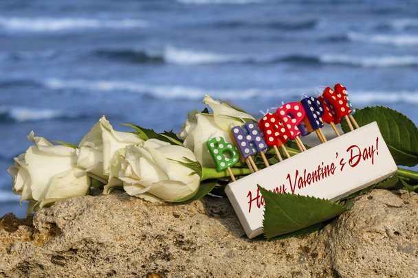caixa de velas com a inscrição "Dia de Valentim feliz" contra umas flores e um fundo do mar
 - Foto, Imagem