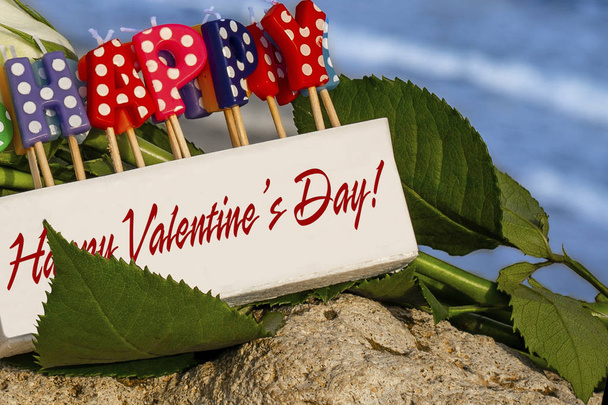 Kerzenschachtel mit der Aufschrift "Happy Valentine 's Day" vor Blumen und Meeresgrund - Foto, Bild