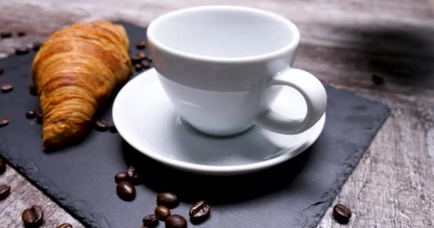 Gießen Sie eine Tasse Kaffee zu einem leckeren Croissant servieren - Filmmaterial, Video