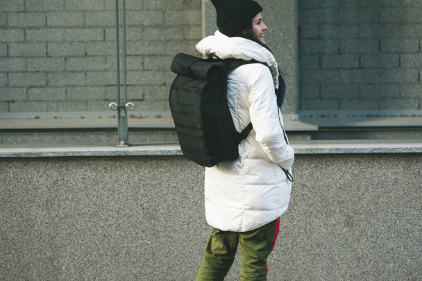 Πλάγια όψη της φοιτήτριας με ένα ζεστό μπουφάν και τσάντα στους ώμους της χαμογελώντας και αναζητούν μακριά - Φωτογραφία, εικόνα