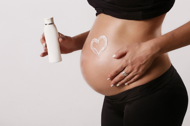 Беременная женщина наносит увлажняющий крем на живот, предотвращая растяжки во время беременности
 - Фото, изображение