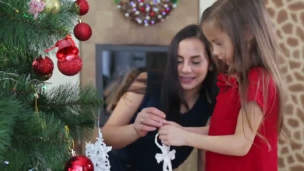 Mother and daughter decorate the Christmas tree for the new year. A woman with a child girl decorates the Christmas tree.  - Кадры, видео