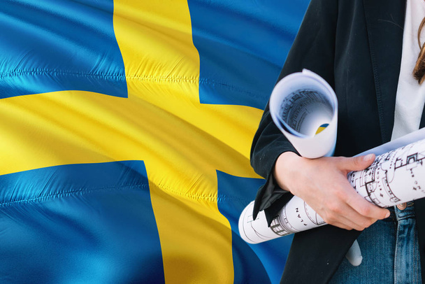 Swedish Architect woman holding blueprint against Sweden waving flag background. Construction and architecture concept. - Foto, Imagen