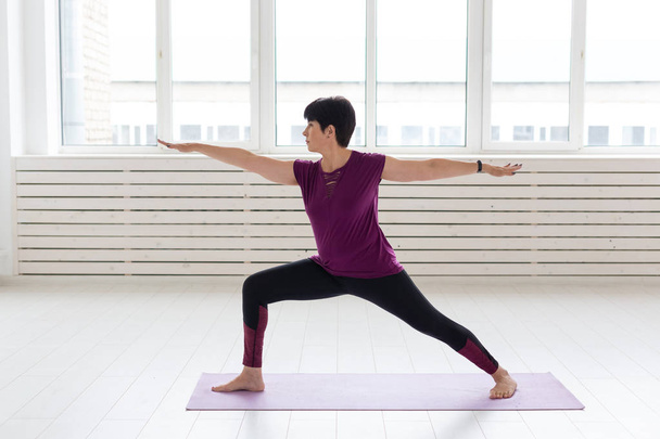 Persone, yoga, sport e assistenza sanitaria concetto donna di mezza età in piedi in guerriero su sfondo bianco
 - Foto, immagini