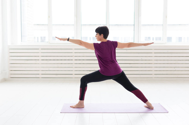 Menschen, Sport und Gesundheitskonzept - Frau mittleren Alters praktiziert Yoga, steht in Krieger zwei Übung - Foto, Bild