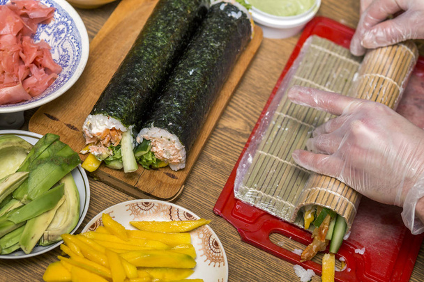 Processus de fabrication de sushis et de rouleaux. Gros plan sur les mains d'un chef cuisinier préparant des plats japonais traditionnels à la maison ou au restaurant sur une table de cuisine
. - Photo, image