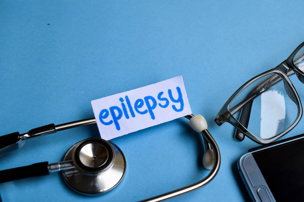 Imagen conceptual con inscripción de epilepsia con la vista del estetoscopio, las gafas y el teléfono inteligente sobre el fondo azul. Conceptual médico
. - Foto, imagen