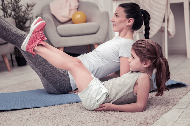 Being a good example for children. A girl joyfully doing exercises with her mother - Foto, Bild