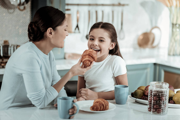 Careful mother feeding a kid with a croissant - Фото, зображення