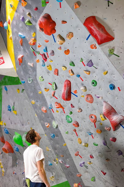 Rock climber stands and looks at the climbing wall with hooks in the boulder hall - 写真・画像