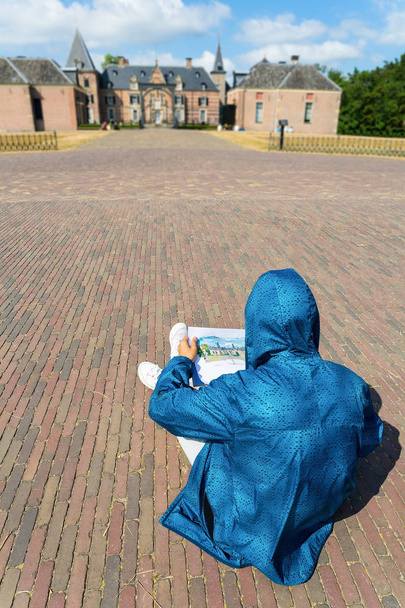 Tiener in blauwe jas zittend op de straat schilderij-kasteel - Foto, afbeelding