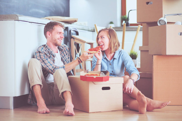 Giovani coppie hanno una pausa pranzo pizza sul pavimento dopo essersi trasferiti in una nuova casa con scatole intorno a loro. Coppia giovane - Foto, immagini