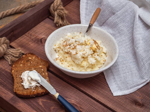 Śniadanie ryż Kasza ryżowa, w głębokim talerzu łyżką z drewnianym uchwytem, grzanki z twarogiem na boardzie rustykalne, serwetka biała bawełna. - Zdjęcie, obraz