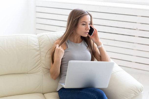 Concepto de negocios, freelance y personas: mujer joven sentada en un sofá y hablando en un teléfono inteligente
 - Foto, imagen