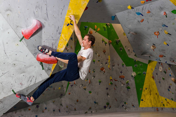 Rock climber man hanging on a bouldering climbing wall, inside on colored hooks - Foto, imagen