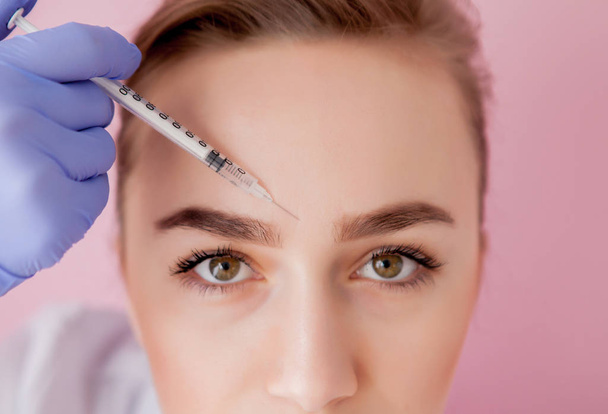 El médico cosmetólogo realiza el procedimiento de inyecciones faciales rejuvenecedoras para apretar y alisar las arrugas en la piel de la cara de una hermosa mujer joven en un salón de belleza.. - Foto, Imagen