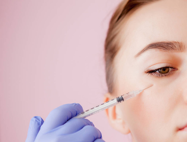 The doctor cosmetologist makes the Botulinotoxin injection procedure for tightening and smoothing wrinkles on the face skin of a beautiful, young woman in a beauty salon.Cosmetology skin care. - 写真・画像