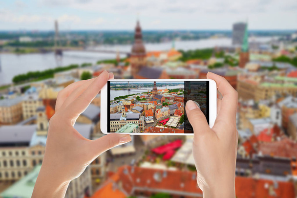 A man is making a photo of panorama of the city of Riga with tilt shift lens on a mobile phone - Photo, Image
