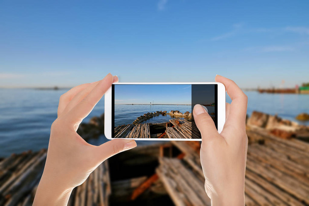 Un uomo sta facendo una foto del paesaggio marino a Tallinn con i resti di una vecchia nave di legno in primo piano su un telefono cellulare
 - Foto, immagini