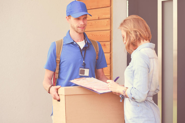 Smiling delivery man in blue uniform delivering parcel box to recipient - courier service concept. Smiling delivery man in blue uniform - Fotoğraf, Görsel