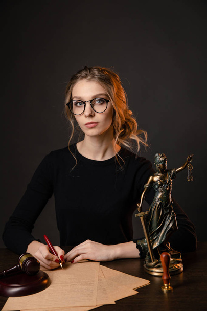 Young lawyer woman in a formal dress and spectacles sitting at table and writing something by pen, lawyer woman with bright red nails working - Photo, Image