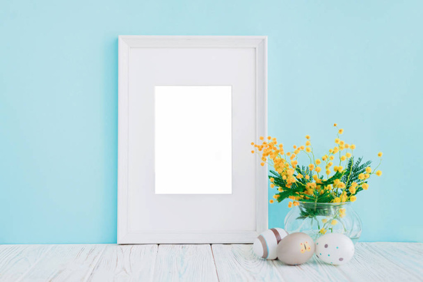 Empty white wooden frame and yellow mimosa flowers on blue background with copy space. Mockup. - Fotografie, Obrázek