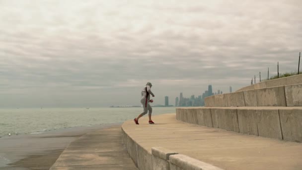 A young athletic man train boxing performs performs jumps on the stairson the stairs exercises against the background of the city and lake, slow motion, - Séquence, vidéo