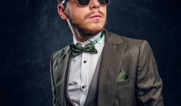 Стильный молодой человек в солнцезащитных очках, одетый в элегантный костюм против темно-текстурной стены
 - Фото, изображение