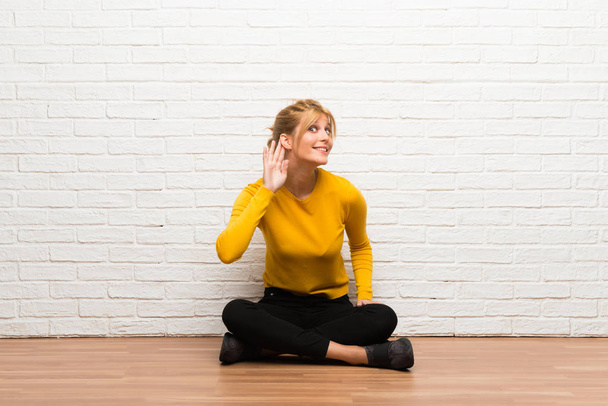 Jeune fille assise sur le sol écoutant quelque chose en mettant la main sur l'oreille
 - Photo, image