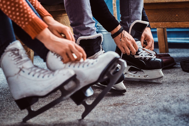 Casal jovem que se prepara para uma patinação. Close-up foto de suas mãos amarrando cadarços de patins de hóquei no gelo no vestiário
 - Foto, Imagem