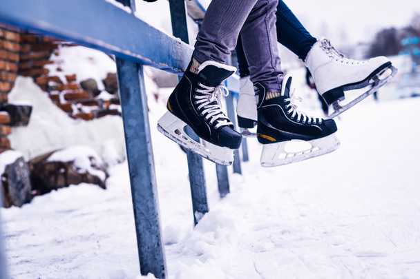 Couple wearing ice skates sitting on a guardrail - Фото, зображення