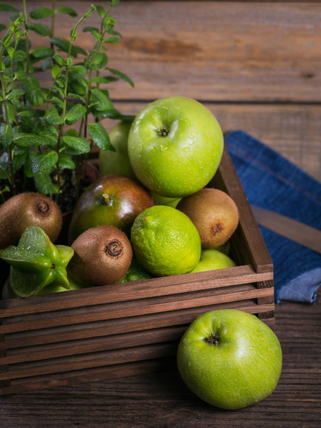 Healthy food background. Concept of healthy food. Fresh green fruits in box on dark wooden background. Set of green fruits for healthy diet and detox: apple, lime, kiwi, mango, carambola and mint. - Φωτογραφία, εικόνα