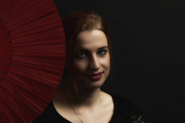 Low Key portrait of seductive young woman holding red fan. All on the dark background. - Fotografie, Obrázek