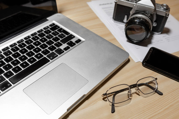 Wooden photographer desk table with camera, laptop, smartphone and eyeglasses - Image - Foto, imagen