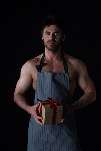 Handsome muscular naked man in an apron holding holiday gift box - Fotoğraf, Görsel