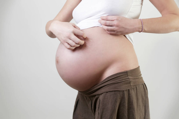 Schwangere kratzt sich am Bauch - Foto, Bild