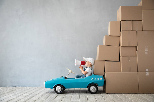 Happy child playing into new home. Kid driving toy car. Moving day concept - Zdjęcie, obraz