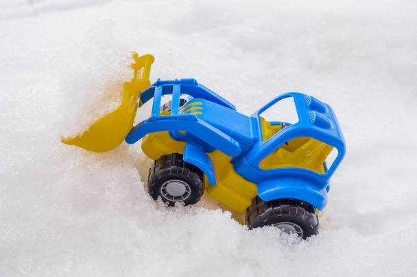 tractor de juguete azul y amarillo de plástico con cargador frontal en la nieve. concepto de utilidades y remoción de nieve. servicios de carreteras
. - Foto, Imagen