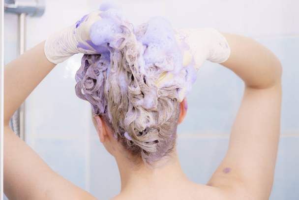 Woman applying coloring shampoo on her hair. Female having purple washing product. Toning blonde color at home. - Fotografie, Obrázek