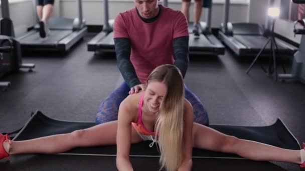 Sportos és vonzó férfi segít egy gyönyörű nő, nyúlik a padlón az edzőteremben. - Felvétel, videó