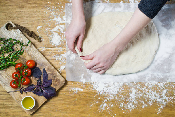 The chef prepares Focaccia. Ingredients for Focaccia: dough, tomatoes, rosemary, thyme, Basil, olive oil on a wooden table. Top view, wooden background - 写真・画像
