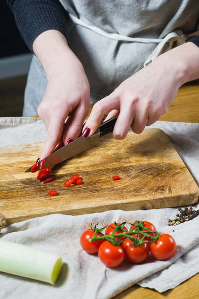 Lo chef taglia peperoncini su un tagliere di legno. Sfondo cucina, vista laterale
 - Foto, immagini