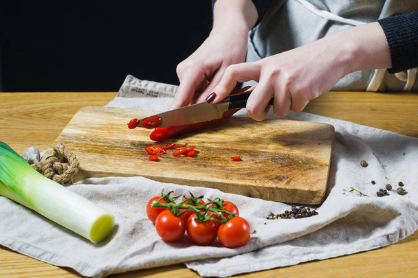 O chef corta pimentas em uma tábua de corte de madeira. Cozinha de fundo, vista lateral
 - Foto, Imagem