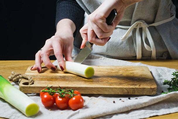 Lo chef taglia porri su un tagliere di legno. Sfondo cucina, vista laterale
 - Foto, immagini