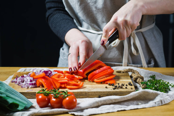 Lo chef taglia i peperoni rossi su un tagliere di legno. Sfondo cucina, vista laterale
 - Foto, immagini
